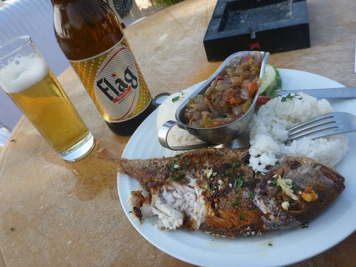Lively beach bar scene with people eating grilled fish and drinking at a West African beach