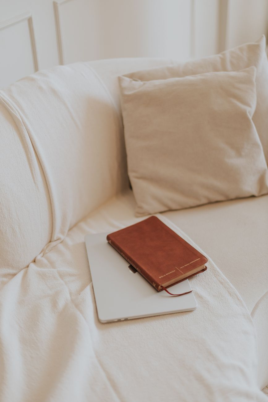 Person journaling Bible study notes next to a tablet showing a reading plan
