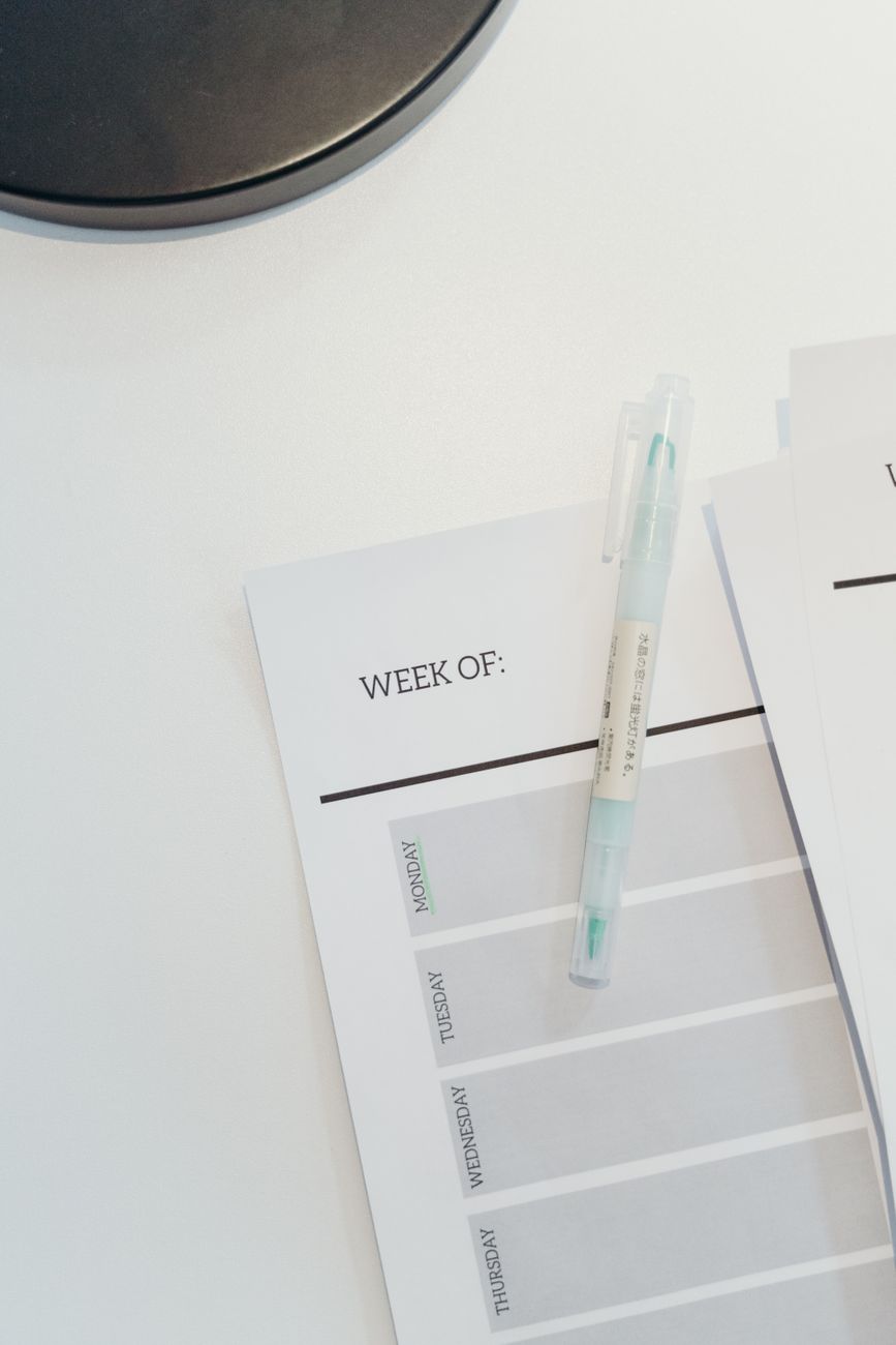 Person writing a weekly schedule in a planner with a coffee cup nearby