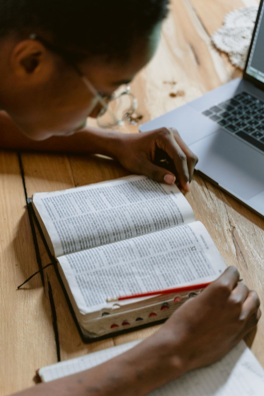 Person studying Bible on a laptop with a notebook open beside them
