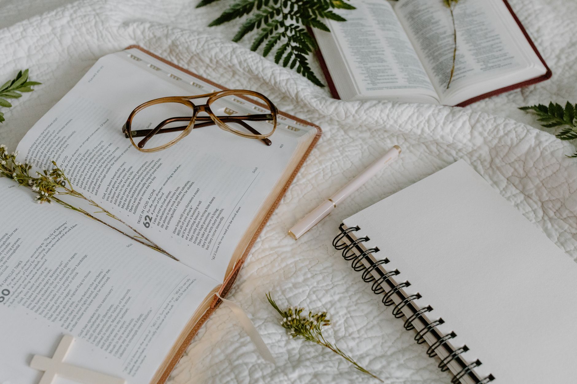 Person writing Bible study notes in a journal next to a smartphone with a Bible app open