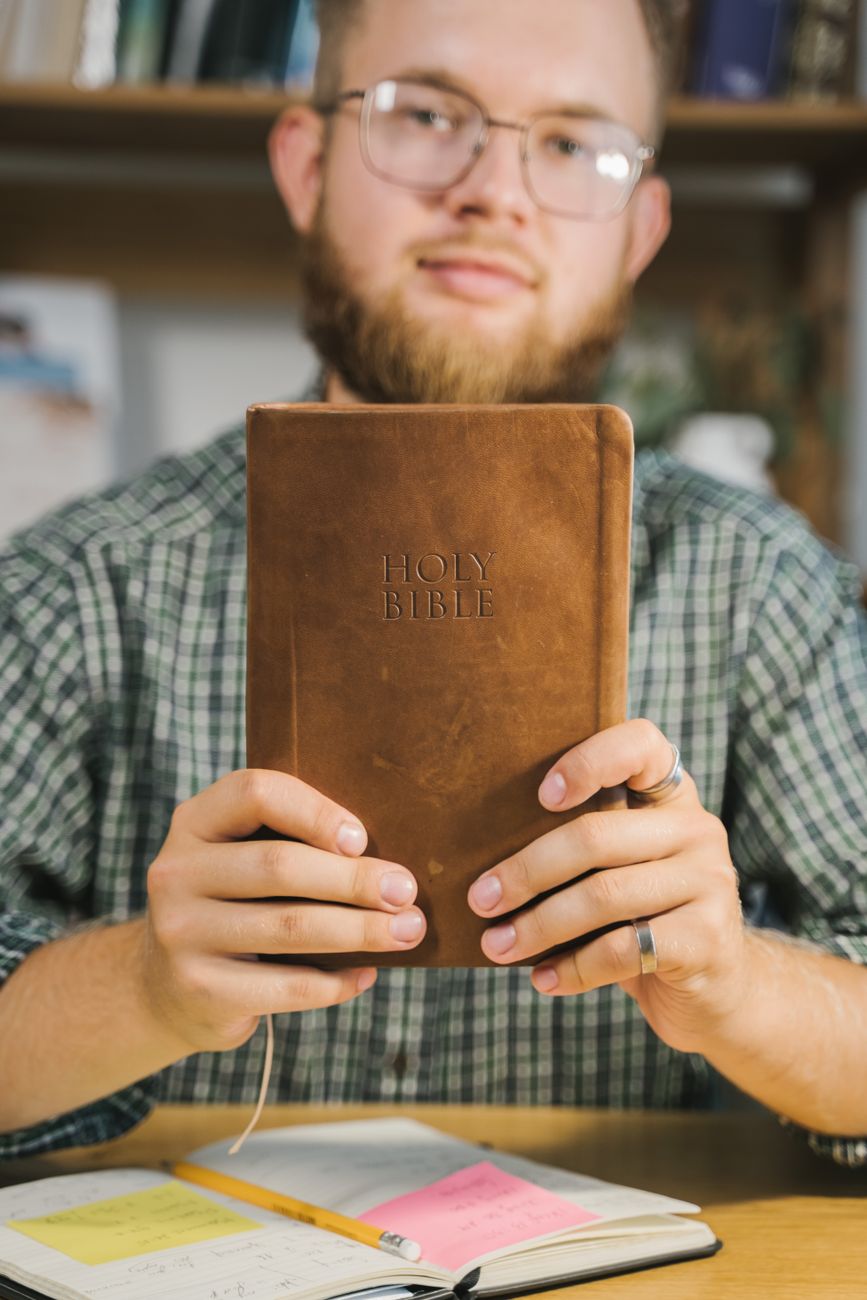 Person reviewing a printed Bible reading plan at a desk with a cup of coffee