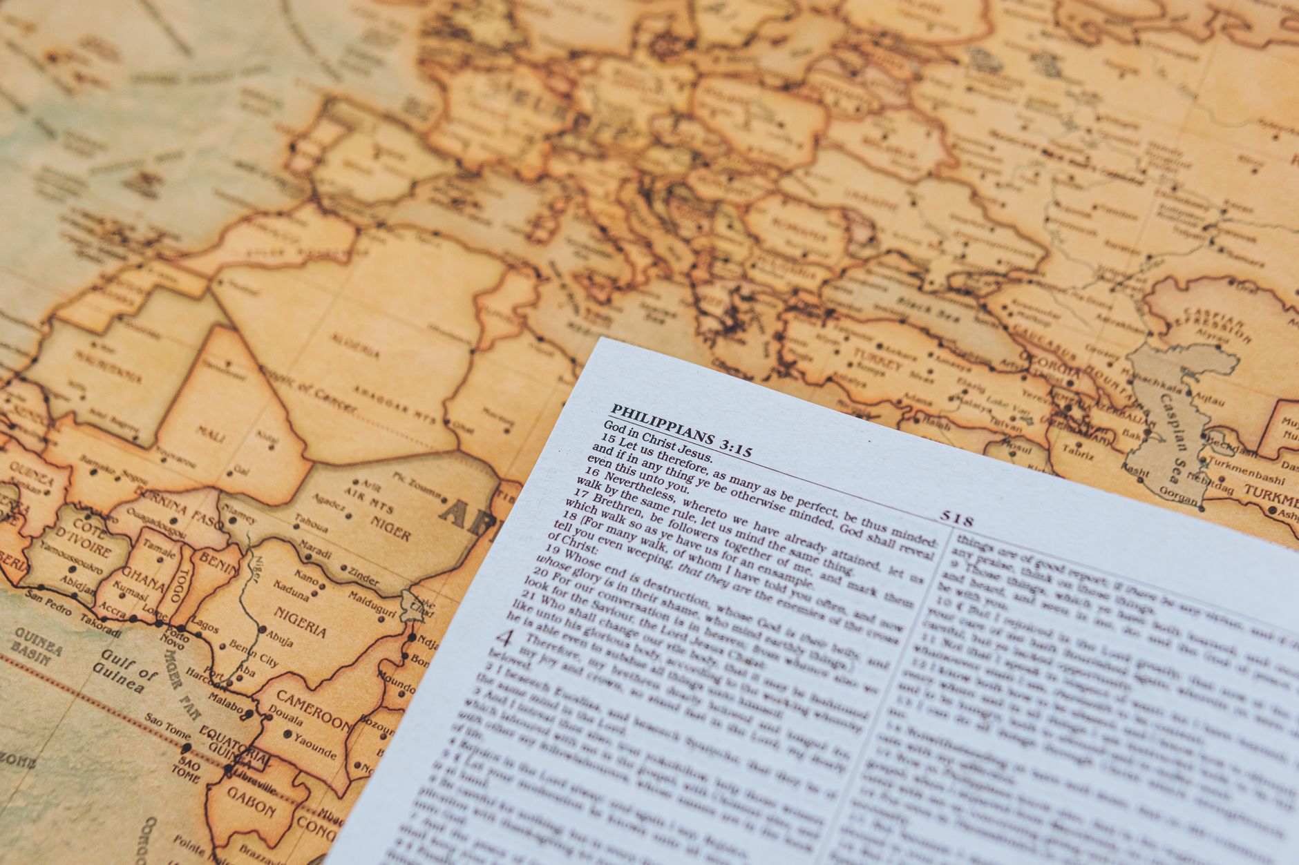 Open Bible with historical maps and study notes spread across a wooden desk