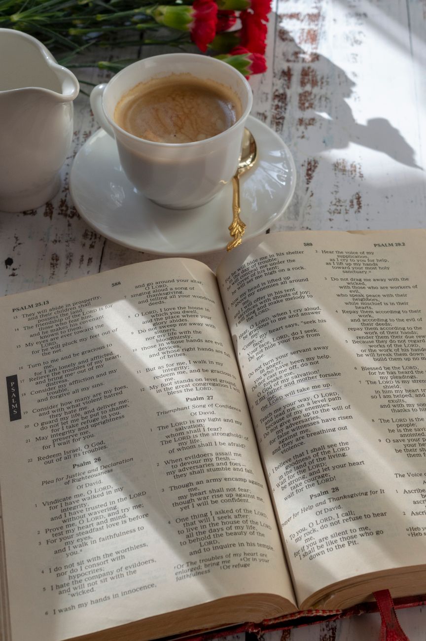 Open Bible on a wooden desk with a coffee mug and journal for morning devotions
