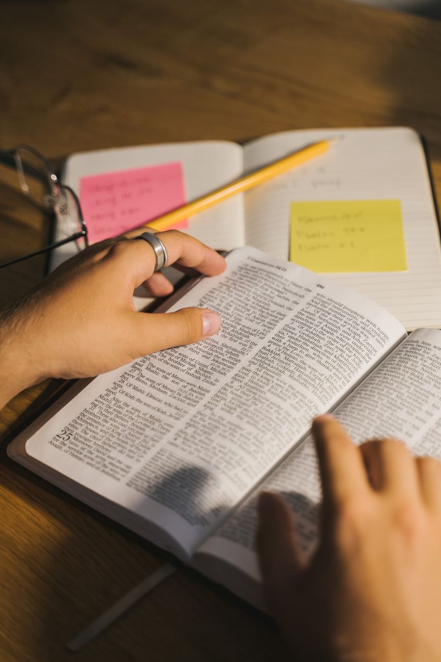 Person reading Bible with a notebook and coffee cup at a desk