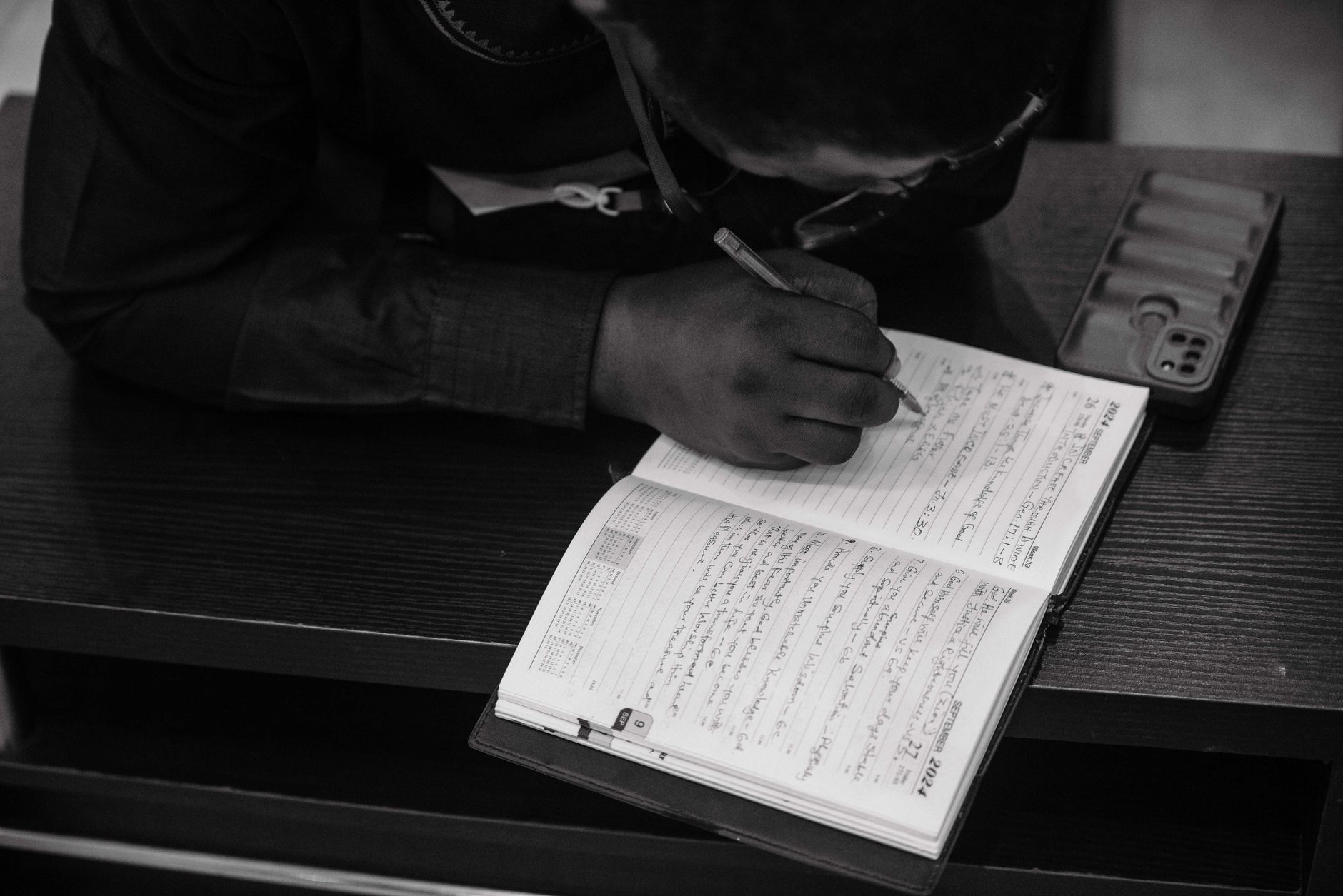 Person reading a Bible with a study notebook and phone open to a Bible app