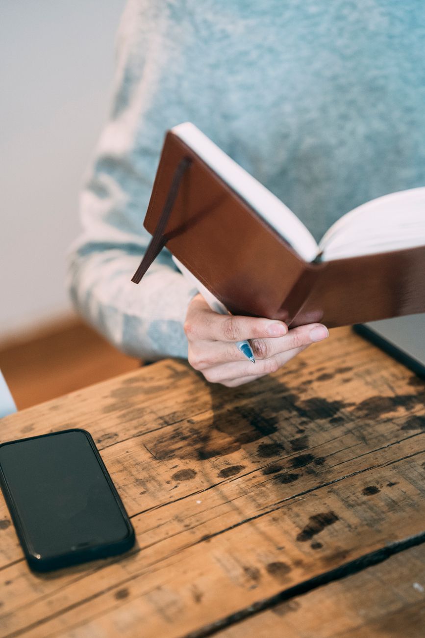 Person studying Bible with a smartphone and open notebook on a wooden desk